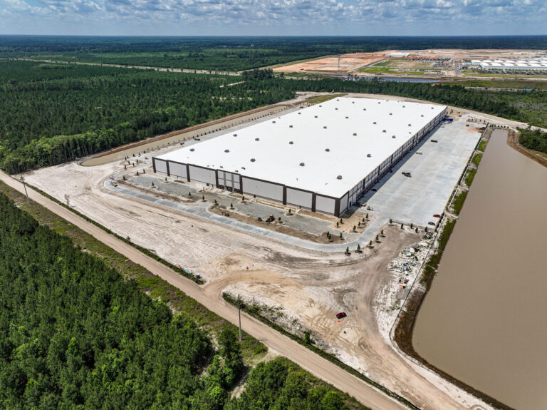 Aerial view of Komar Distribution warehouse under construction surrounded by greenery and a pond