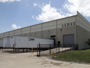 Komar Distribution warehouse loading dock with trucks and clear sky